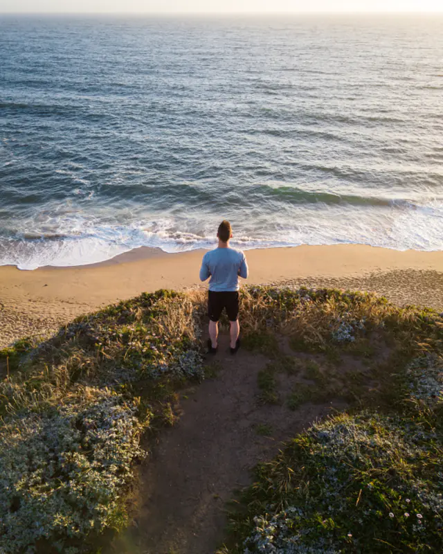 A man standing on a grassy cliff path, looking calmly out to sea