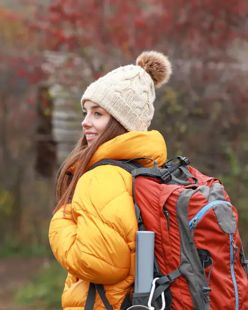 A smiling woman with a rucksack walking through autumn woodland