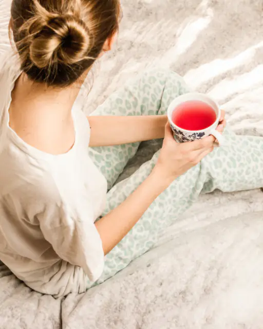 A woman winding down in bed with a cup of tea