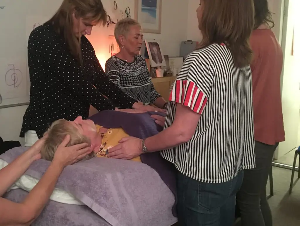 A person lying on a treatment couch while practitioners practise Reiki hand positions